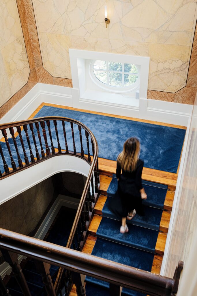 Hóspede descendo a luxuosa escadaria de madeira clássica com passadeira azul-royal deste hotel boutique no Porto.
