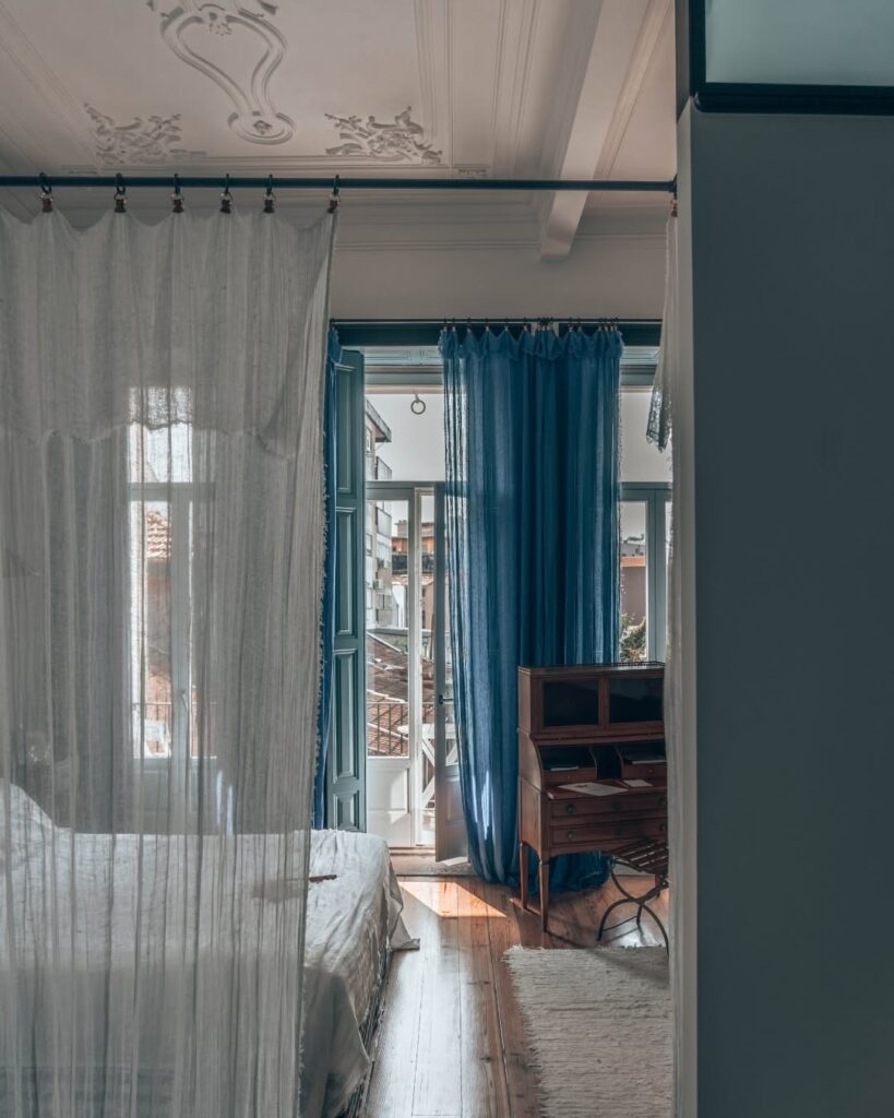 Quarto com dossel de linho e escrivaninha de madeira clássica sob teto decorado no Cocorico Luxury House, um elegante hotel boutique no Porto.