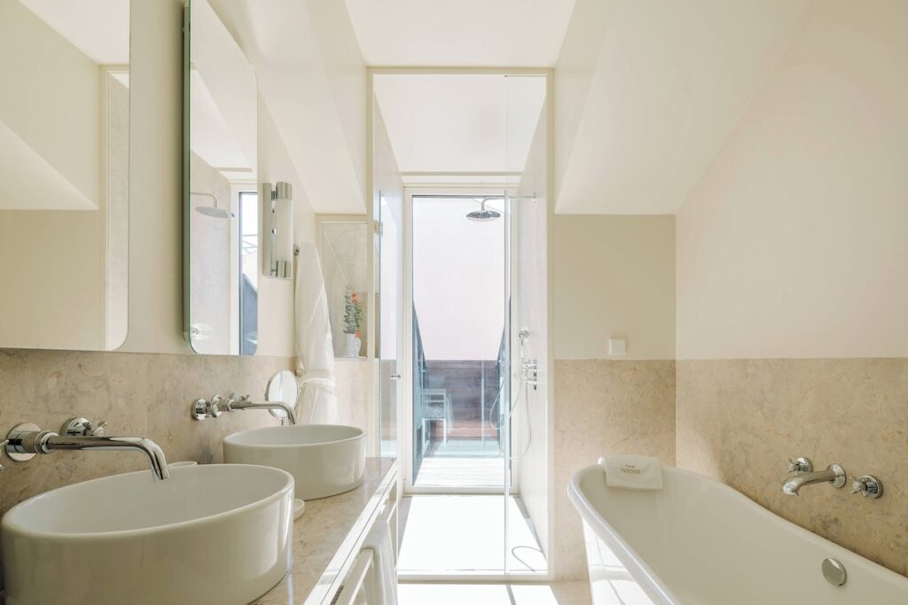 Banheiro de ático no The Ivens Hotel com cubas redondas, banheira e porta de vidro para varanda, requinte nos hoteis boutique em lisboa.