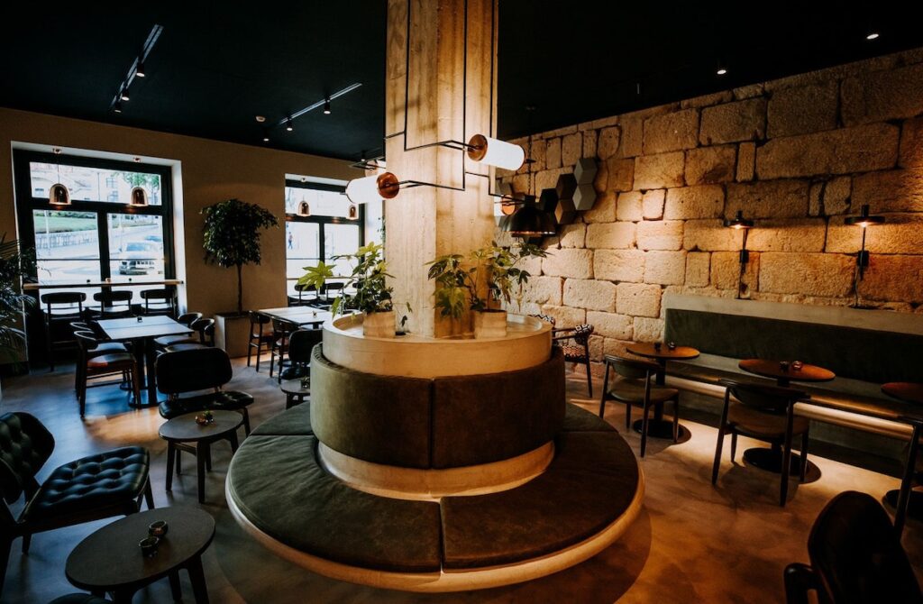 Elegante bar de hotel boutique no Porto com banco circular de veludo verde, teto preto, iluminação intimista e parede de pedra rústica original.