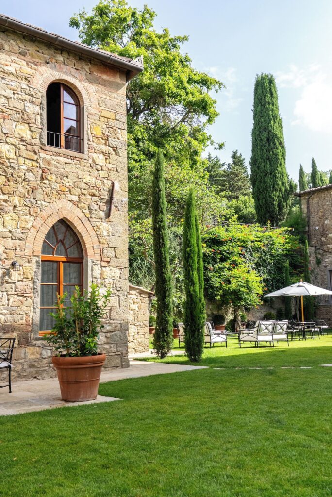Fachada medieval de pedra e ciprestes clássicos no jardim do Pieve Aldina, cenário inesquecível de lua de mel na europa.