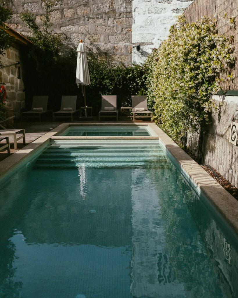 Piscina externa cercada por deck de madeira e parede com trepadeira florida no Torel Saboaria, um dos melhores hotéis boutique no Porto.