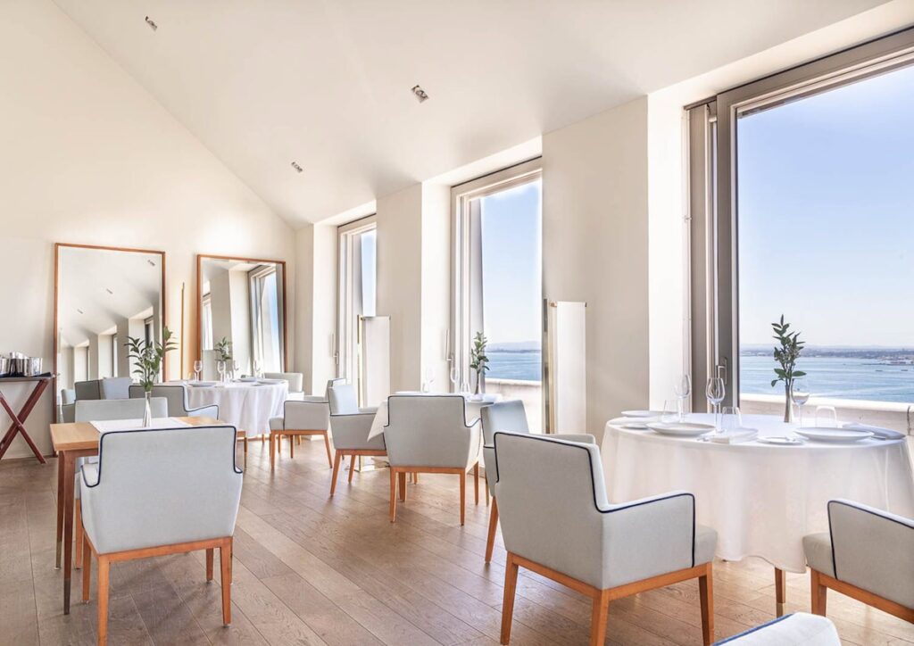 Restaurante panorâmico no Verride Palácio Santa Catarina com mesas postas, toalhas brancas e vista do Rio Tejo, destaque de hoteis boutique em lisboa.