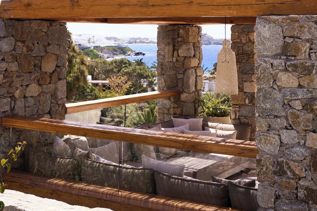 Lounge externo de pedra natural com sofás rebaixados e vista para o mar Egeu na Villa de luxo do resort em Mykonos.