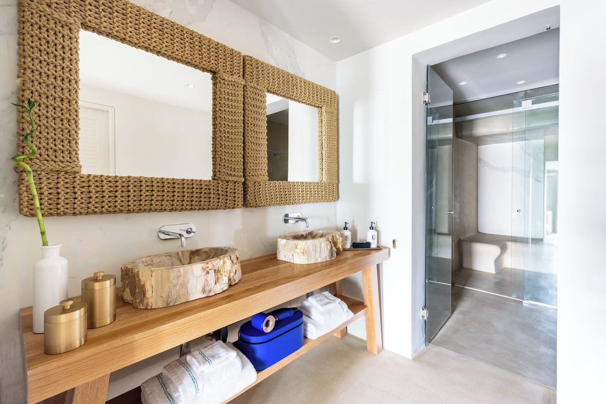 Banheiro de luxo com cubas de madeira petrificada e espelhos de corda no Nammos Hotel, resort em Mykonos focado em design de autor.