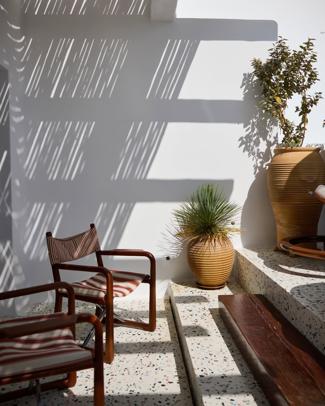 Jogo de luz e sombra em terraço com cadeiras listradas da Loro Piana no Nammos Hotel, sofisticado resort em Mykonos.