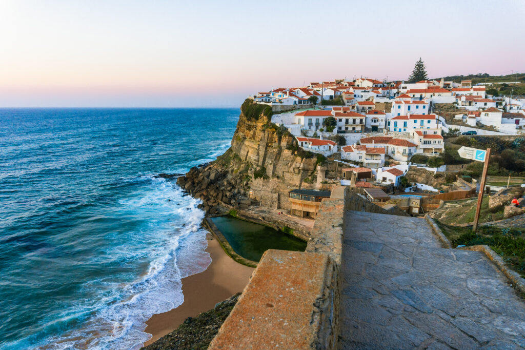 Casario branco de Azenhas do Mar em Sintra sob o crepúsculo na melhor época para visitar portugal, com piscina natural e praia.
