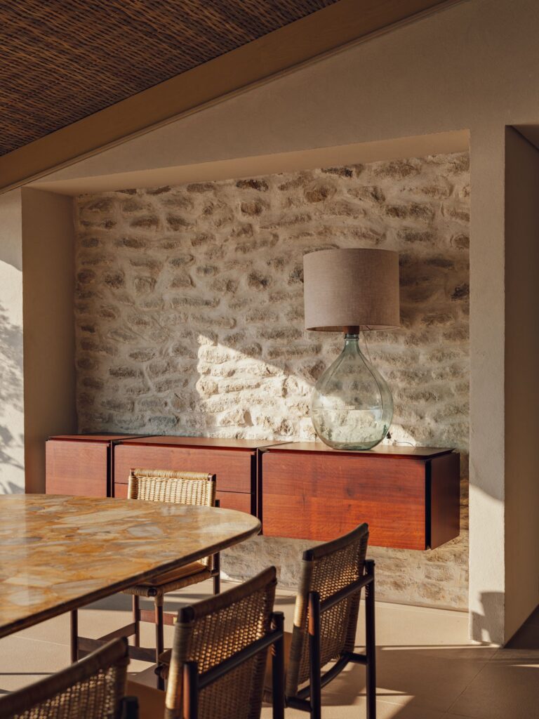 Sala de jantar com parede de pedras brutas, aparador de madeira escura e cadeiras de palhinha, revelando decoração aconchegante de inverno.