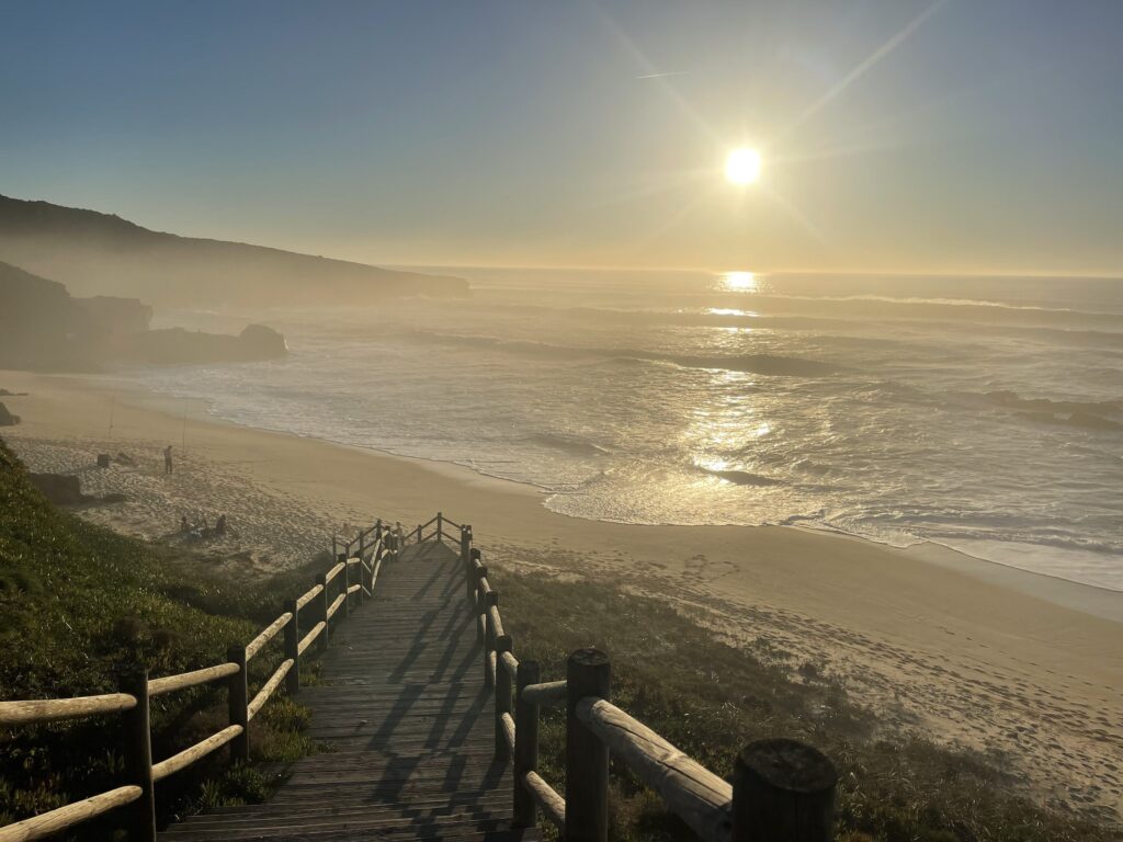 Passarela de madeira na praia de Malhadinhas, em Vila Nova de Milfontes, durante a melhor época para visitar portugal no pôr do sol.