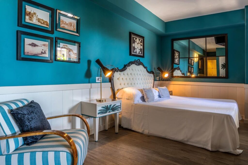 Quarto no Hotel Villa Carlotta, uma referência de hotéis boutique na sicilia, com parede azul-turquesa e poltrona listrada.