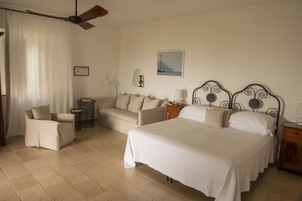 Quarto clássico do Hotel Signum, um dos charmosos hotéis boutique na sicilia, com cabeceira de ferro forjado e piso de pedra clara.