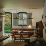 Sala de estar integrada com mesa de jantar de madeira e detalhes coloniais na Pousada Liter&aacute;ria de Paraty, com remos decorativos e jardim ao fundo.