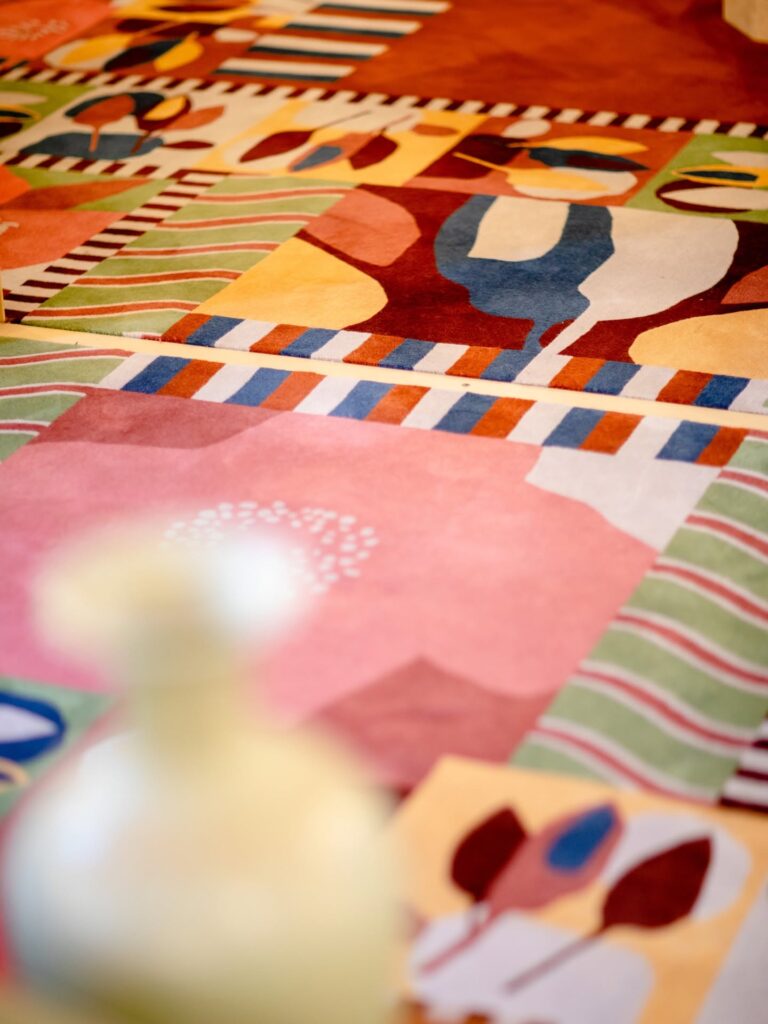 Detalhe do carpete colorido com formas geométricas abstratas projetado para o Palazzo Talìa, destacando tons de rosa, verde e amarelo.