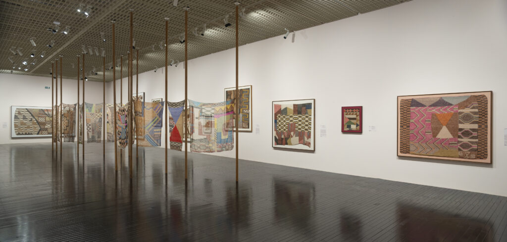 Painéis de madeira sustentando obras têxteis coloridas no MASP, parte das exposições em São Paulo que trazem texturas artesanais para o design.