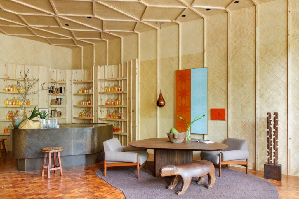 Bar e mesa orgânica no Living Ritmo Vital da MAAI na Casacor 2026 com painéis de palha e estante artesanal.