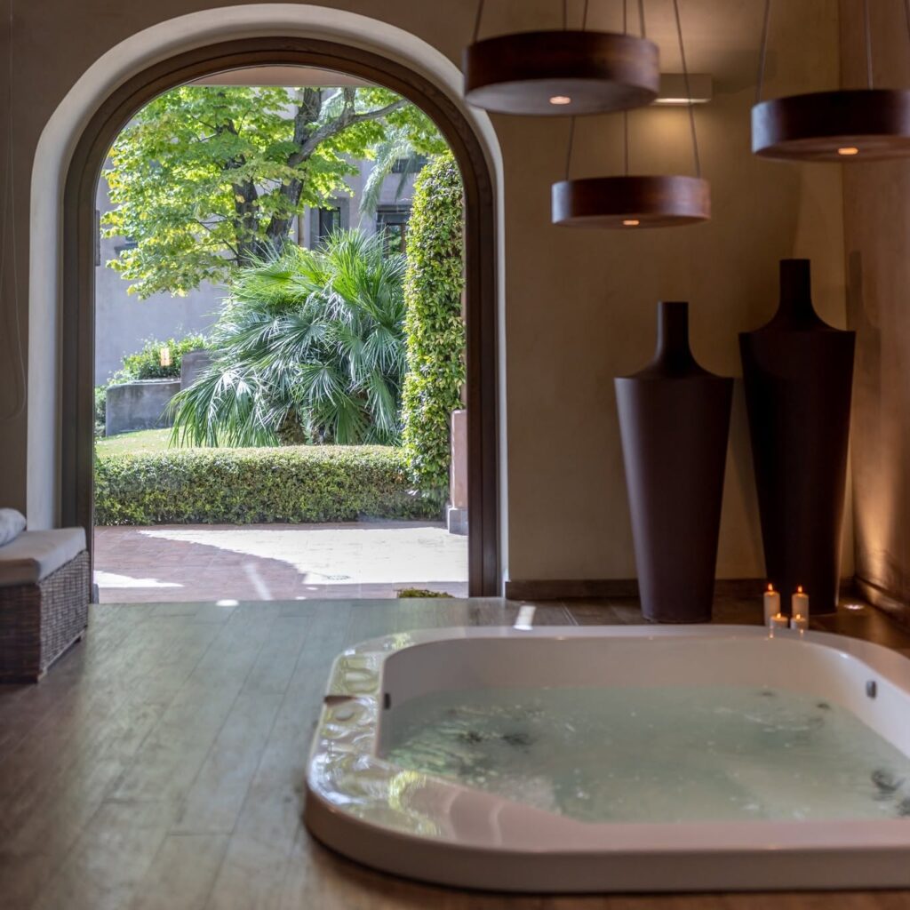Spa com banheira de hidromassagem embutida, vasos monumentais e abertura arqueada para o jardim no Relais San Giuliano na Sicília.