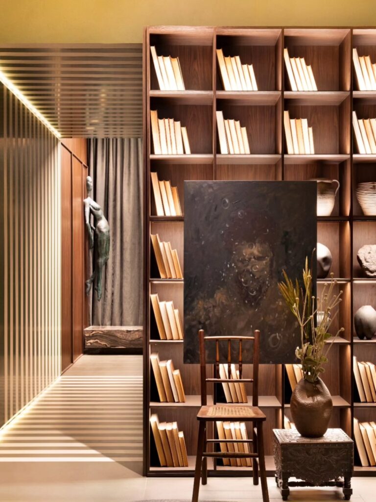Estante de madeira com livros retroiluminados e cadeira vintage no espaço Banheiro da Saudade Casacor 2026.