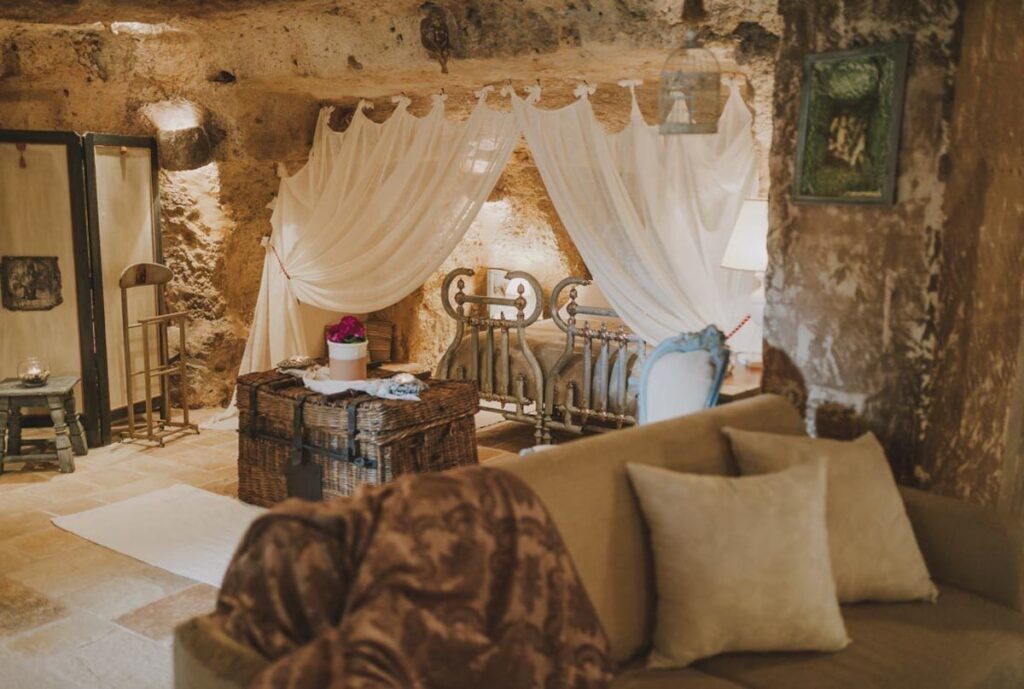 Quarto de casal escavado em rocha na Masseria Montenapoleone com cama de ferro e dossel fluido.