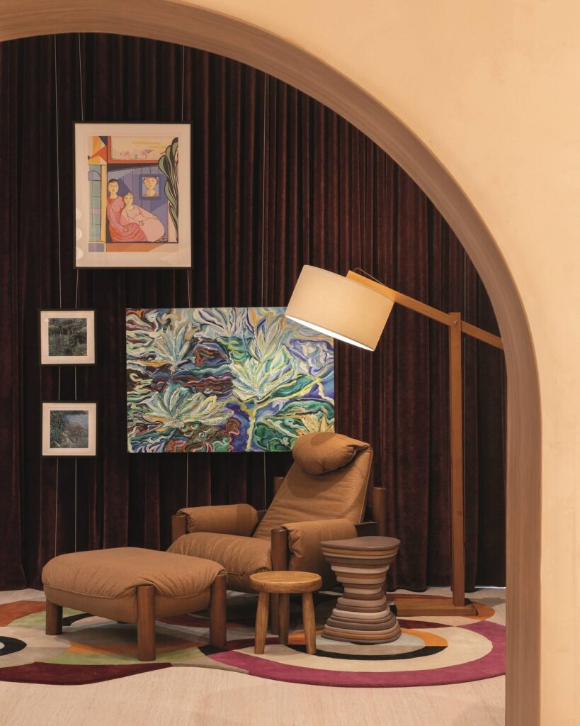 Cantinho de leitura do Qalb Boutique Café na CasaCor 2026 com poltrona acolhedora, tapete artístico colorido e cortinas de veludo.