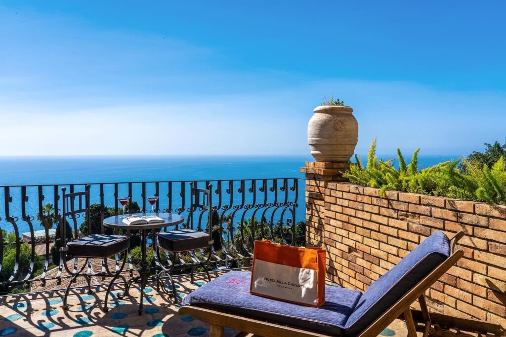 Terraço privativo com piso de majólica, espreguiçadeira azul e vista para o mar no Hotel Villa Carlotta Taormina na Sicília.
