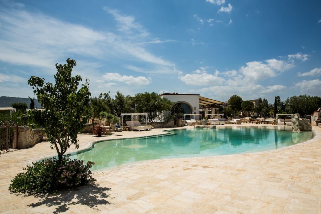 Piscina de desenho orgânico cercada por deque de pedra e vegetação na Masseria Montenapoleone.
