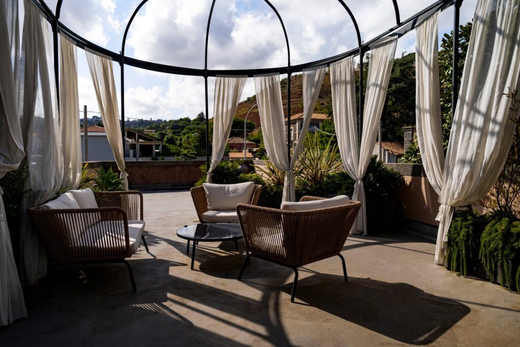 Terraço lounge sob gazebo circular com cortinas de linho e móveis de corda náutica no Relais San Giuliano na Sicília.