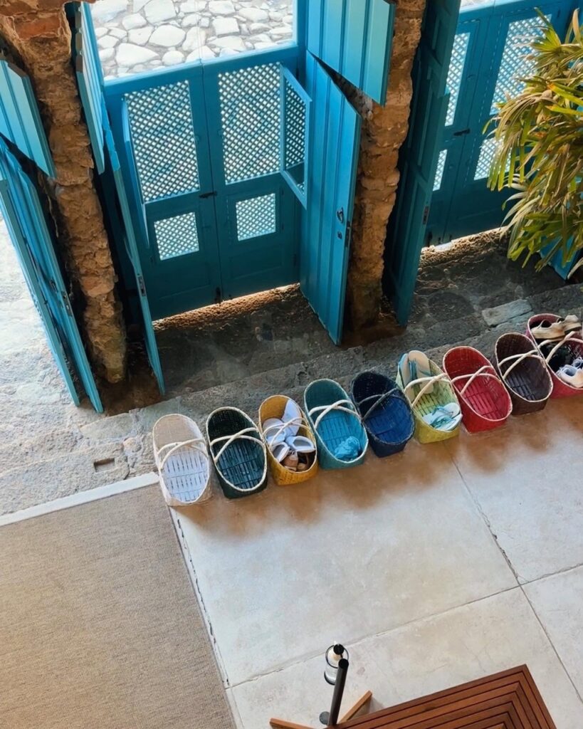 Hall de entrada da Casa Turquesa Maison d'Hôtes com portas de muxarabi azuis, arcos de pedra e cestos de vime coloridos com chinelos para hóspedes.