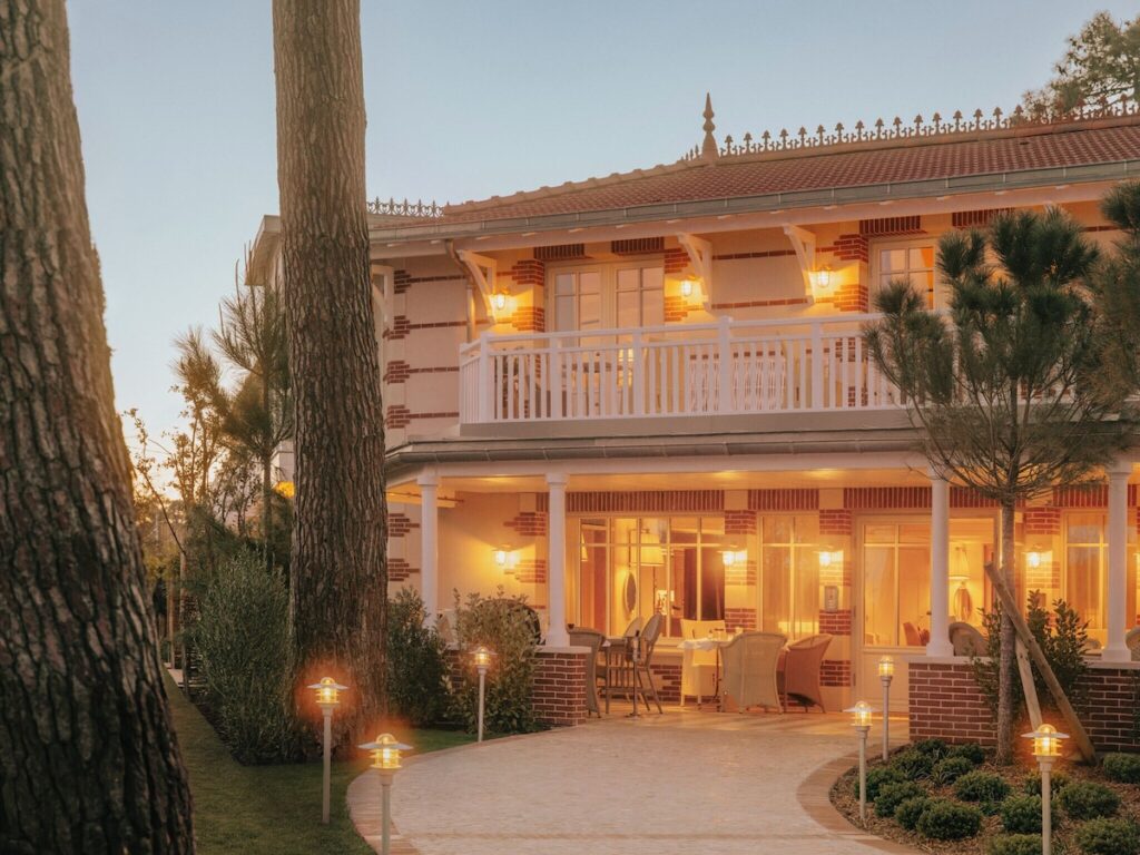 Fachada neo-século XIX iluminada ao anoitecer do hôtel villa colette com varanda branca, colunas e pinheiros característicos da península.
