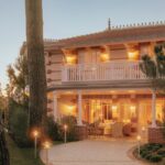 Fachada neo-s&eacute;culo XIX iluminada ao anoitecer do h&ocirc;tel villa colette com varanda branca, colunas e pinheiros caracter&iacute;sticos da pen&iacute;nsula.