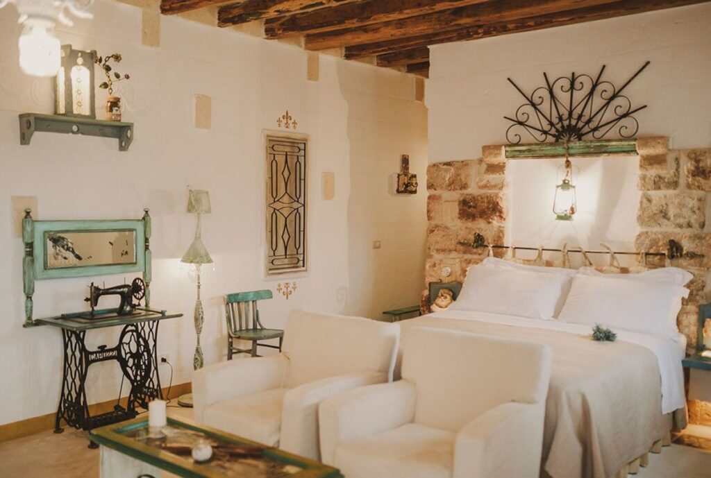 Quarto triplo na Masseria Montenapoleone com paredes de pedra, móveis de upcycling e linho claro.