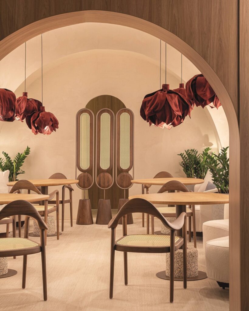 Salão de refeições do Qalb Boutique Café na CasaCor 2026 sob abóbada com pendentes em formato de pétalas vinho e cadeiras em palhinha.