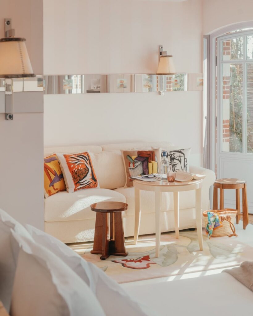 Detalhe de sala de estar íntima com sofá de bouclé beige, almofadas coloridas e mesa de madeira no hôtel villa colette.