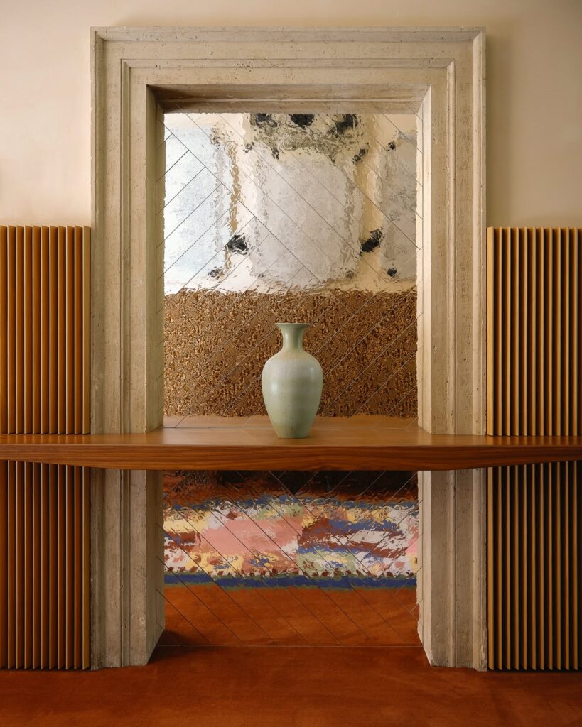 Portal de travertino com prateleira de madeira, vaso verde e fundo espelhado em losangos no Palazzo Talìa.