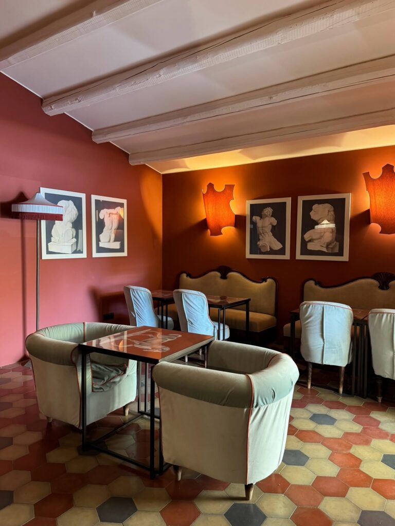 Bistrô com parede vermelha pompeiana, piso de ladrilhos hexagonais e poltronas de veludo no Q92 Noto Hotel na Sicília.