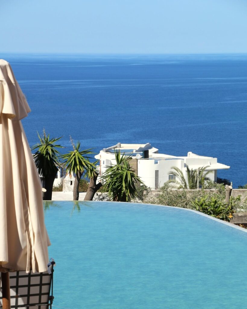 Piscina de borda infinita com vista para o mar azul e vegetação tropical no Hotel Signum Salina na Sicília.