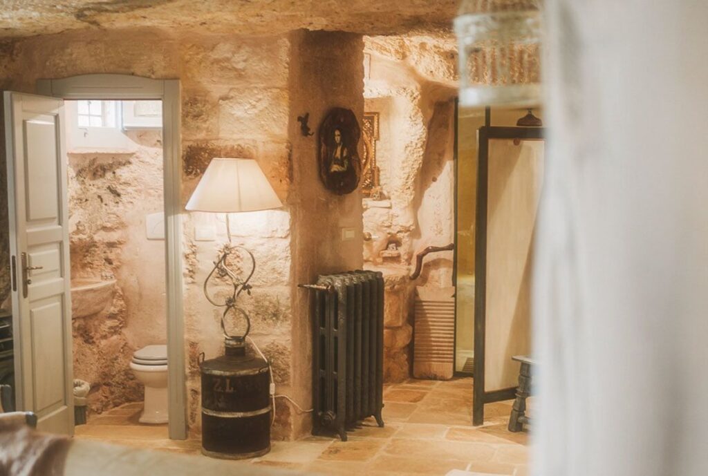Interior de quarto romântico escavado em rocha na Masseria Montenapoleone com luz quente.