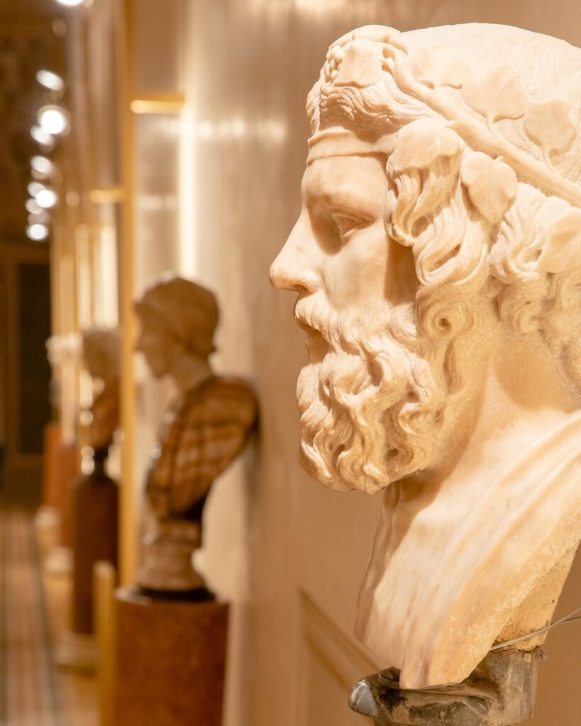 Busto clássico de mármore romano exposto sobre pedestal de madeira no corredor do hotel Palazzo Talìa.