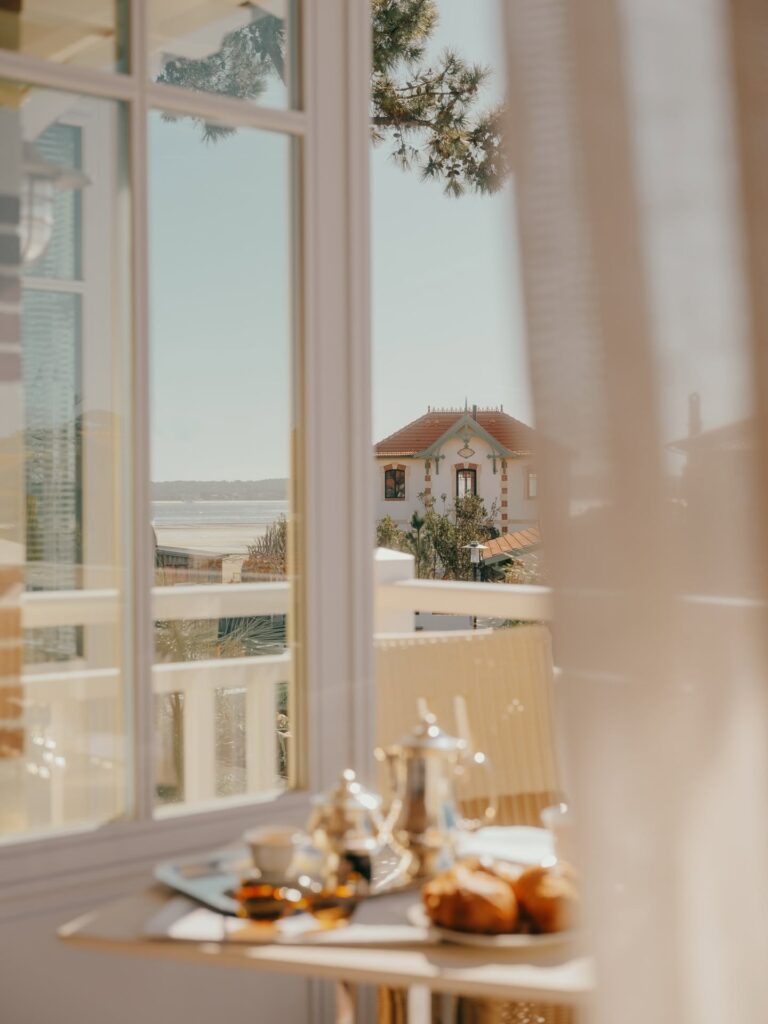 Vista de café da manhã em mesa de madeira através da janela de vidro do hôtel villa colette, avistando o mar da Bacia de Arcachon.