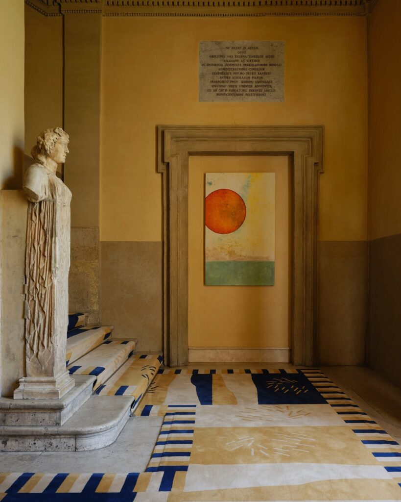 Patamar de escada histórica no Palazzo Talìa com estátua de mármore, carpete geométrico e tela abstrata moderna.