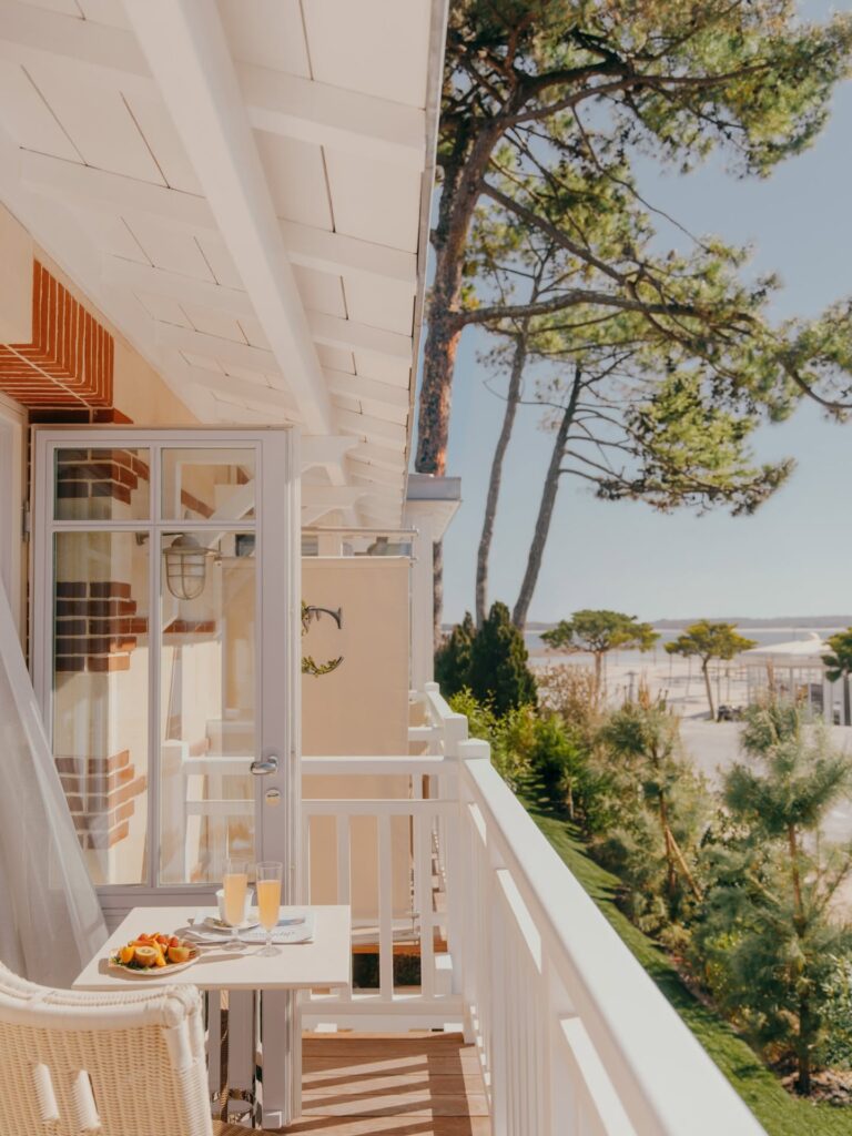 Varanda de quarto com café da manhã e vista para pinheiros e a baía de Cap Ferret, integrando o hotel com a deslumbrante natureza local.