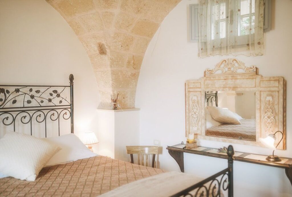 Quarto quádruplo sob arco de pedra com cama de ferro forjado na Masseria Montenapoleone.
