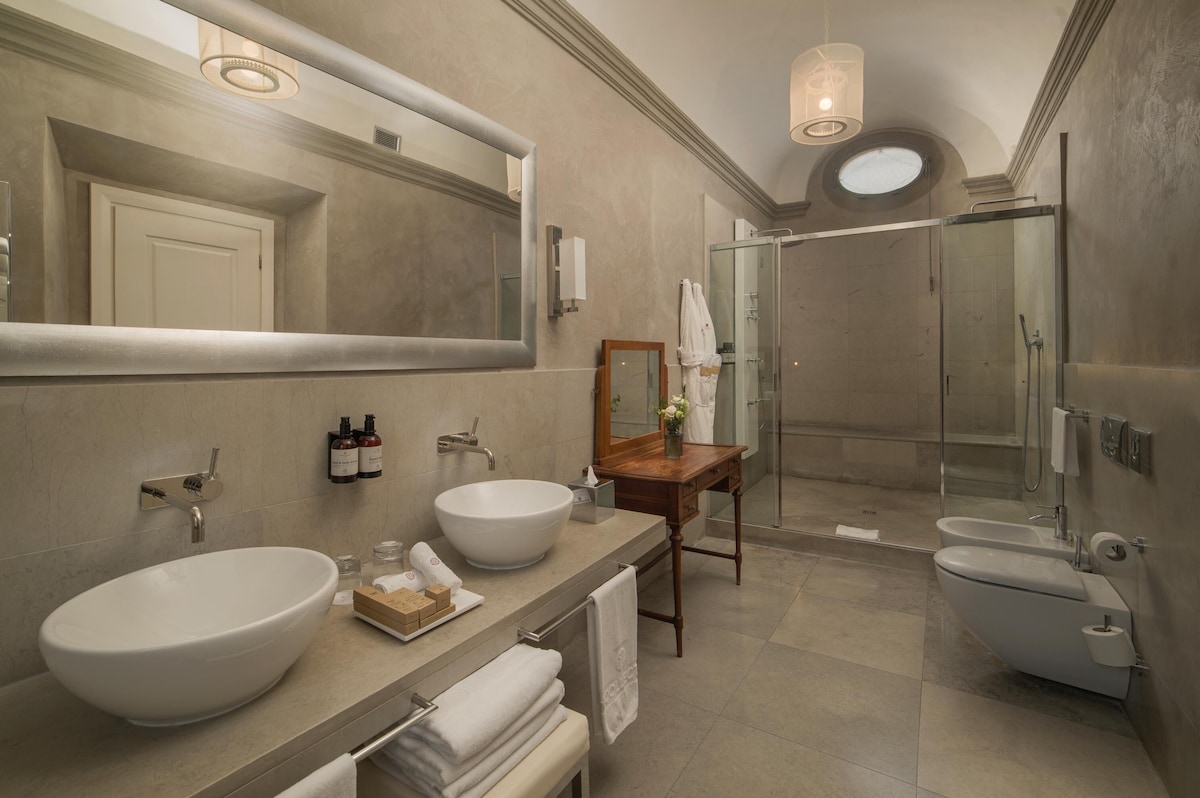 Banheiro luxuoso da Torrigiani Junior Suite no Porta Rossa com teto abobadado, pedra cinza, cuba dupla moderna e penteadeira vintage em madeira.