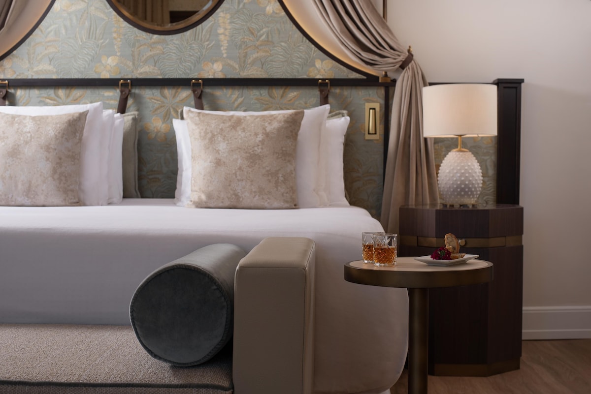 Salimbeni Junior Suite no Porta Rossa com detalhe de cama de dossel contemporâneo, cabeceira botânica e criado-mudo hexagonal escuro com luminária branca.