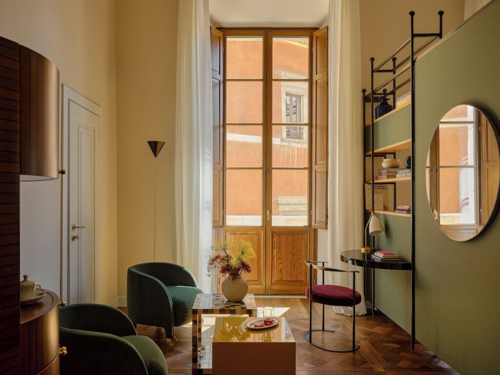 Decoração da Suíte Standart do Palazzo Talìa com poltronas de veludo verde, piso de madeira e mesa amarela.