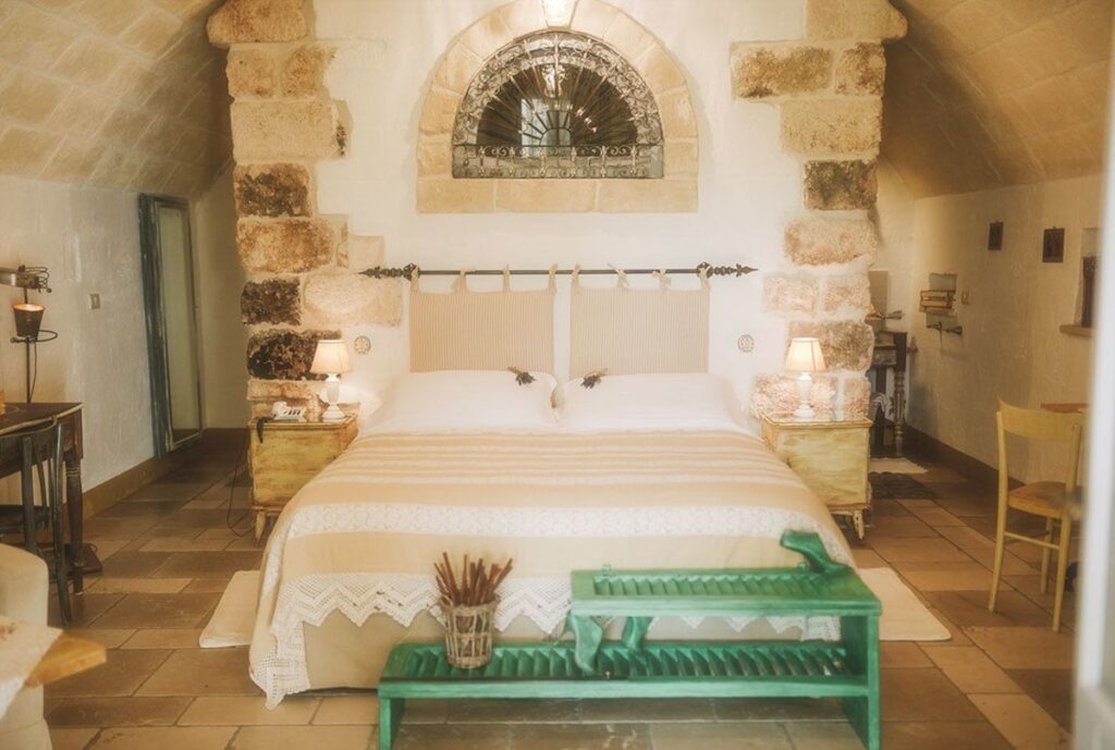 Quarto triplo com parede de pedra destacada e banco verde-menta na Masseria Montenapoleone.