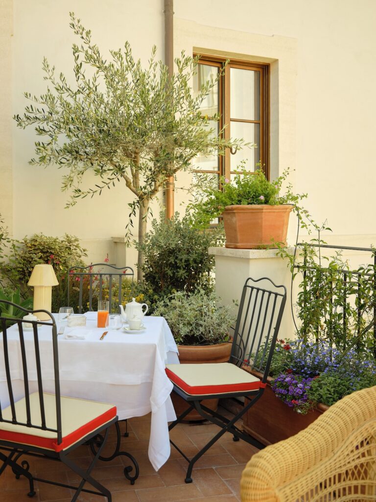 Mesa de café da manhã posta em terraço ensolarado e florido da Suíte Panorâmica do hotel Palazzo Talìa Roma.