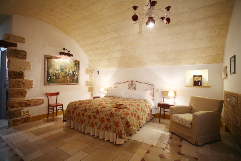 Quarto de casal abobadado com colcha floral e piso de pedra na Masseria Montenapoleone.