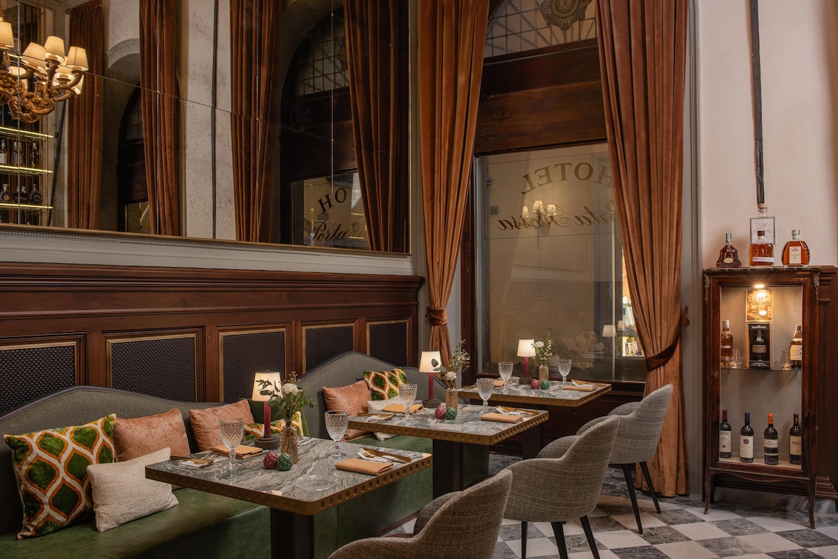 Restaurante do Porta Rossa com mesas de mármore, assentos de couro verde oliva, cortinas de veludo terracota e amplos painéis de espelhos envelhecidos.