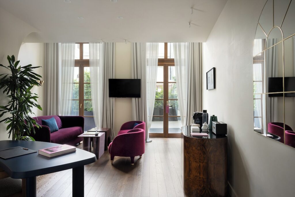 Sala de estar elegante da Suíte Premium no Palazzo Talìa, com móveis de veludo roxo, aparador de nogueira e espelho.
