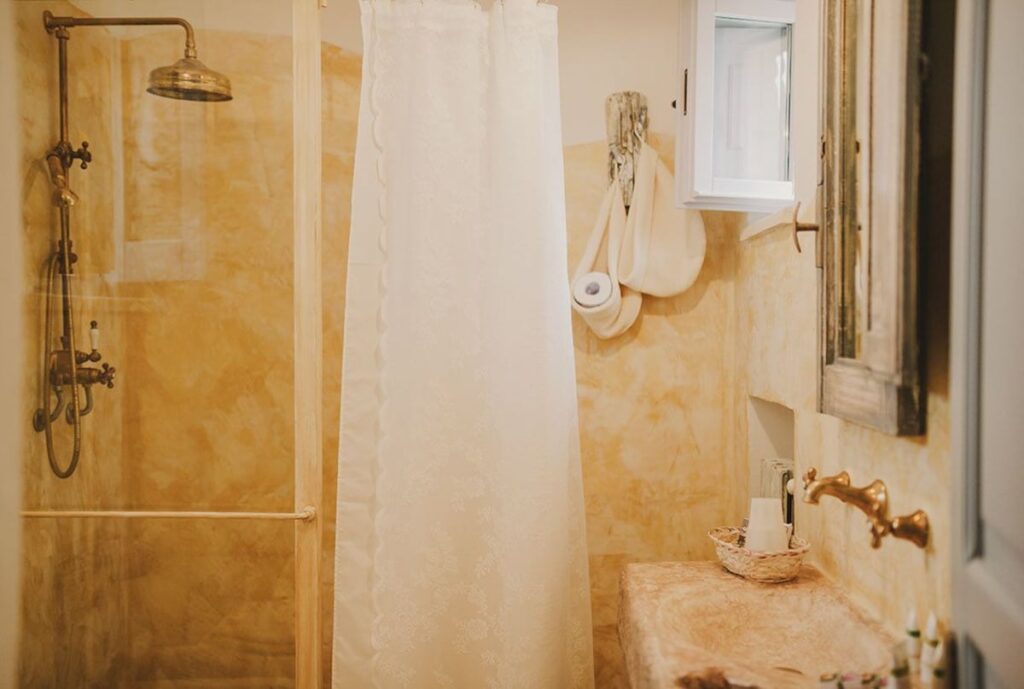 Banheiro da suíte superior na Masseria Montenapoleone com chuveiro em latão e parede amarela.